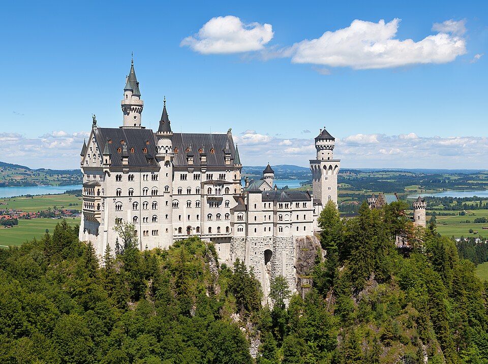 Schloss Neuschwanstein auf seinem bewaldeten Bergrücken über Hohenschwangau und dem Alpenvorland.